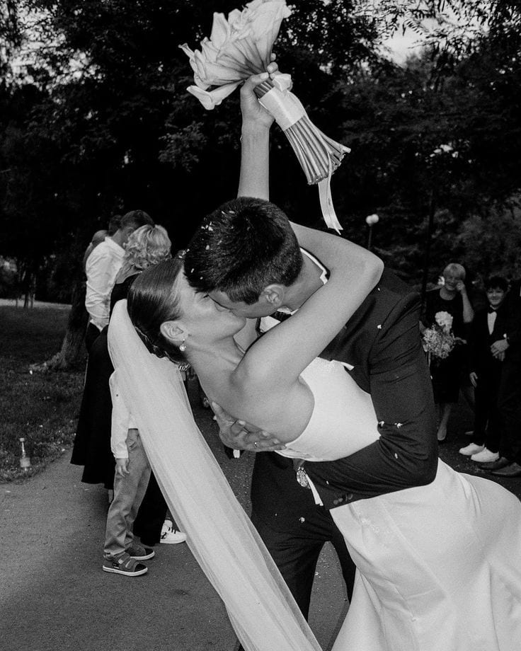 Couple kissing behind the bridal bouquet, in black and white