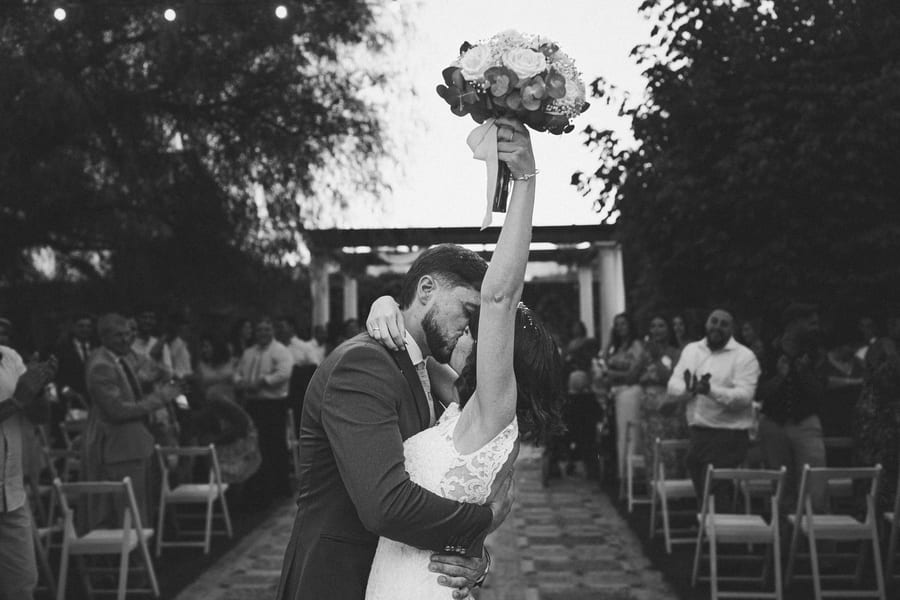 Couple kissing during an outdoor ceremony, in black and white